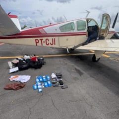 Foto mostra avião monomotor numa pista de asfalto com barras de ouro em sacos plásticos espalhadas no chão