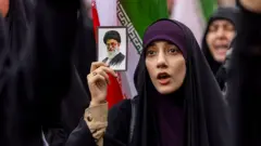 အီရန်ကို အမေရိကန်နဲ့အစ္စရေးတို့တိုက်ခိုက်မှုကို ဖေဖော်ဝါရီလ ၂၈ ရက်မှာ တီဟီရန်မြို့မှာ ပြုလုပ်တဲ့ဆန္ဒပြပွဲအတွင်း ခါမေနီရဲ့ဓာတ်ပုံကိုင်ထားတဲ့ အီရန်အမျိုးသမီးတစ်ဦး 