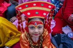 ইন্দ্রযাত্রার সময় কুমারি পূজায় এক শিশুকে লাল পোশাকে দেবী রূপে সাজানো হয়েছে, শিশুটি মুখ তুলে তাকিয়ে হাসছে