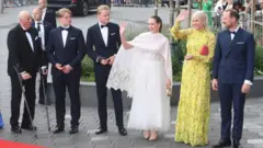 Dos mujeres, la princesa Ingrid Alexandra con un vestido blanco y la princesa Mette-Marit con un vestido amarillo, aparecen con cuatro hombres, entre ellos el rey Harald a la izquierda y Marius Borg Høiby a la izquierda de su hermana Ingrid Alexandra.
