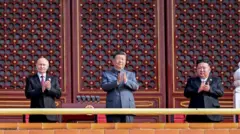 시진핑 중국 국가주석 오른편에 블라디미르 푸틴 러시아 대통령이, 왼편에는 김정은 북한 국무위원장이 서 있다. 2025년 9월 3일 중국 베이징에서 열린 전승절 80주년 기념 군사 퍼레이드에 참석를 박수를 치는 모습 