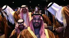 محمد بن سلمان، ولیعهد عربستان سعودی، در کنار اعضای هیئت سعودی در «همایش سرمایه‌گذاری آمریکا–عربستان» در مرکز جان اف. کندی در واشنگتن دی‌سی در ۱۹ نوامبر ۲۰۲۵. او آماده می‌شود تا به سخنرانی دونالد ترامپ، رئیس‌جمهور آمریکا گوش دهد.