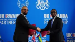 Minisitiri w'ubutegetsi bw'igihugu w'Ubwongereza James Cleverly (ibumoso) asuhuzanya na Minisitiri w'ububanyi n'amahanga w'u Rwanda Vincent Biruta, nyuma yo gusinya amasezerano mashya ku bimukira, aha ni i Kigali, ku itariki ya 5 Ukuboza (12) mu 2023