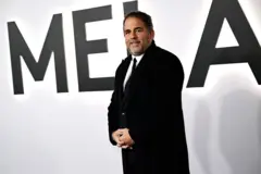 Brett Ratner usando um sobretudo preto. Ele está em pé.