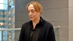 Ayşe Barım adliye koridorunda üzerinde siyah ceketle ayakta duruyor