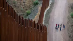 Migrantes procedentes de Centroamérica y Sudamérica, que buscan asilo, caminan junto a la valla fronteriza tras haber cruzado ilegalmente hacia Estados Unidos el 24 de junio de 2024 en Ruby, Arizona.