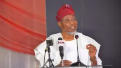Rauf Aregbesola n sọrọ, o wọ agbada funfun ati fila pupa