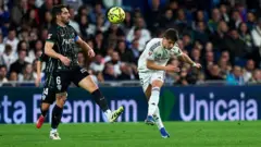 Arda Güler topun dibine doğru giriyor ve yanında bir rakip oyuncu varken vuruş yapıyor.