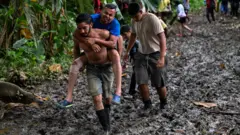 Un hombre carga en su espalda a otro mientras atraviesan el Darién.