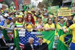 Dezenas de pessoas com roupas verde e amarelas; uma pessoa segura bandeira com foto de Bolsonaro e Trump juntos, e montagem com bandeiras dos EUA e Brasil juntas; é possível ver também cartazes com dizeres como 'SOS Trump' e 'Eleição sem Bolsonaro é ditadura'