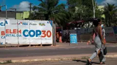 Ayol iqlim bo'yicha konferentsiyani e'lon qiluvchi plakat yonidan o'tmoqda.