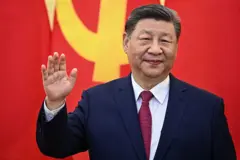 El presidente chino, Xi Jinping, saluda con la mano derecha, con una bandera china detrás. 