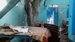 Sala de aula destruída, com as paredes perfuradas por balas