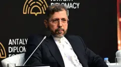 Saeed Khatibzadeh sério durante evento, ao lado de microfone e sentado