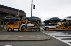 Un camión de carga transporta vehículos nuevos en una calle de México