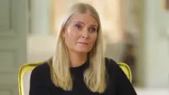 A blonde-haired in a black sweater looks on the verge of tears