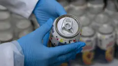 Membro da Polícia Judiciária portuguesa mostra uma lata aberta de suco de pêssego confiscada que contém cocaína, no dia 20 de maio de 2024, em Lisboa, Portugal