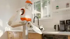 Sunday AI's Memo robot holds a plate in the kitchen and prepares to place it in the dishwasher