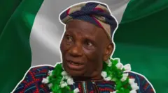 A man wearing a garland of green and white flowers and a traditional cap on his head looking to the right of the photo.