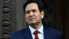 O secretário de Estado dos EUA, Marco Rubio, observa sua chegada ao Quai d'Orsay vestindo um blazer, camisa branca e gravata.
