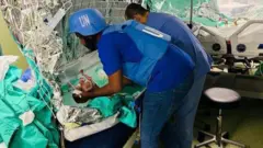 Un trabajador de la ONU traslada un bebé en sus brazos 