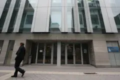 Fachada moderna de vidrio y concreto con varias puertas de entrada y una persona caminando por la acera