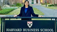 Shreya Mishra Reddy stands behind a sign with the words Harvard Business School and a crest of the institution at its campus in Boston in the United States.