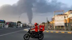 Seorang pengantar barang sedang melihat kepulan asap tinggi membumbung dari ledakan di zona industri Fujairah (03/03). Perang Iran yang diawali serangan AS-Israel, memaksa UEA menutup wilayah udaranya.