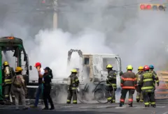 Membros do Corpo de Bombeiros de Guadalajara trabalham para extinguir um incêndio que envolve vários veículos em Guadalajara, no México, em 22 de fevereiro de 2026. Um caminhão e um ônibus estão em chamas, cercados por um grande grupo de bombeiros.