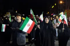 Mulher rezando com bandeira do Irã