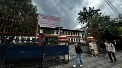 राष्ट्रिय अभिलेखालय बाहिरको दृश्य। सडक पेटीमा युवाहरू हिँडिरहेको देख्न सकिन्छ। एक जना सेतो सर्ट र खाकी रङ्गको पेन्ट लगाएका युवा अभिलेखालय भवनभित्र जान लाग्दैछन्