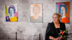 Королева Нидерландов Беатрикс с букетом цветов в руках стоит на фоне трех своих молодых портретов работы Энди Уорхола