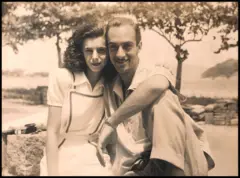 Dias Gomes e Janete Clair sentados próximos com a baía da Guanabara ao fundo, em foto em preto e branco