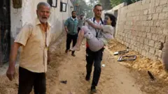 Ahitwa Khan Younis muri Gaza umugabo atwaye umwana w'umunyepalestina wakomeretse nyuma y'igisasu cya Israel  