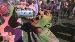 Homem bebe cerveja diretamente de uma lata durante uma festa, cercado por outras pessoas e sob luzes coloridas.