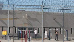Cercados pelas grades e pela concertina de arame, diversos detidos podem ser vistos no pátio do centro de processamento do ICE em Adelanto, no Estado americano da Califórnia, no dia 11 de julho de 2025