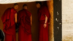 سه راهب با لباس‌های قرمز در یک ردیف ایستاده‌اند و با هم صحبت می‌کنند، صورت‌هایشان را از دوربین برگردانده‌اند