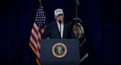 ټرمپ دریځ ته ولاړ لیدل کېږي سپینه خولۍ یې پر سر ده.