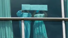 पनामा के होटल की खिड़की पर खड़ी दो लड़कियां मदद की अपील करती हुईं