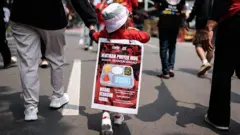 Seorang anak berusia 3 tahun dari anggota Aliansi Gerakan Reforma Agraria (AGRA) membentangkan spanduk di punggungnya yang menentang program makan gratis (MBG) saat demonstrasi pada Hari Tani Nasional di Jakarta pada 24 September 2025.