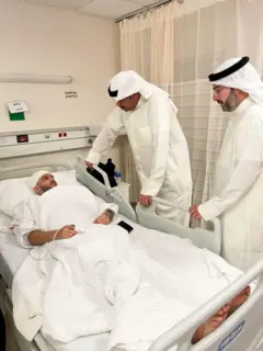 El ministro de Defensa kuwaití, el jeque Abdullah Ali Abdullah al Salem al Sabah, un hombre con túnica blanca mira a una persona en una cama, con la cabeza con vendas.