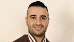 عمّار الحويطات في صورة قديمة مرتدياً قميصاً رياضياً يبدو أنه بني اللون. بشرته حنطية وعيناه وشعره لونهم أسود.