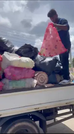 ලොරියක ප්ලාස්ටික් බෝතල් සහ කෑන් මලු තුළ දමා පැටවා ඇති අතර පුද්ගලයෙකු ප්ලාස්ටික් බෝතල් අඩංගු මල්ලක් එල්ලගෙන සිටියි.