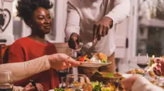 Pessoas à mesa em uma refeição, com um homem servindo um pedaço de ave para outra pessoa