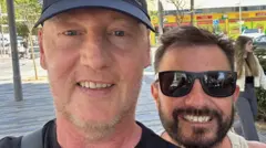 Dois homens sorriem em uma selfie em uma rua na Espanha