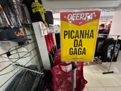 Uma placa com os dizeres Oferta: Picanha da Gaga em loja de roupa