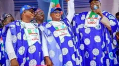 Awọn ọmọ ẹgbẹ ose;u APC fa ọwọ oludije gomina nipinlẹ Osun, Bola Oyebamiji soke gẹgẹ bii oludije wọn. Gbogbo wọn wọ ankara alawọ buluu ti wọn ya aworan oludije gomina APC naa si ati fila rẹ