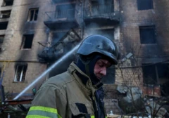 Muškarac u spasilačkoj uniformi pored spaljene zgrade