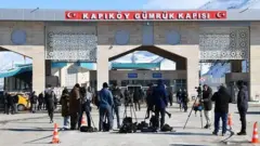 Van'daki Kapıköy sınır kapısında çekilmiş bir fotoğraf. gümrük kapısı önünde gazeteciler ve ekipmanları gözüküyor. Arkada bazı insanlar yürüyor.