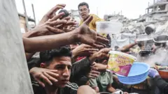 Displaced Palestinians hold out pans at a community kitchen in Jabalia refugee camp, northern Gaza (24 April 2025)